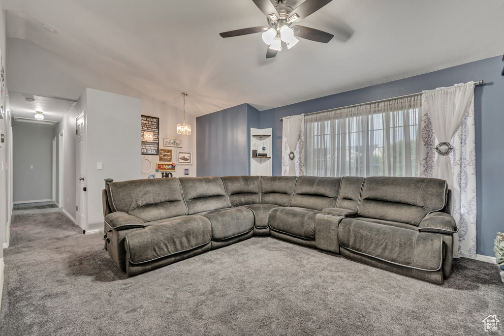 Carpeted living room featuring ceiling fan, a chandelier, and baseboards