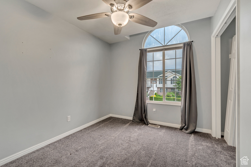 Spare room featuring healthy amount of natural light, carpet flooring, ceiling fan, and baseboards