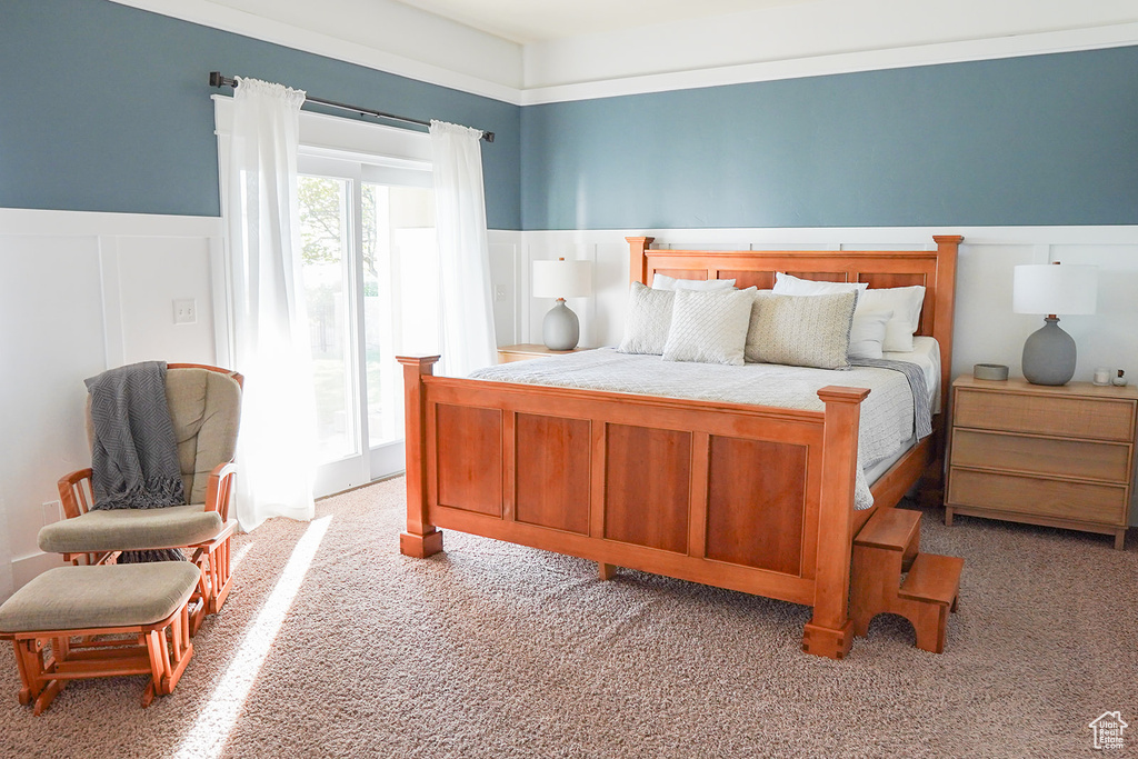 Bedroom featuring light carpet, access to outside, wainscoting, and a decorative wall