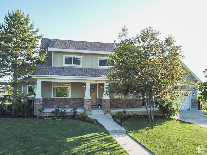 View of front of property featuring covered porch, stone siding, a front lawn, and board and batten siding