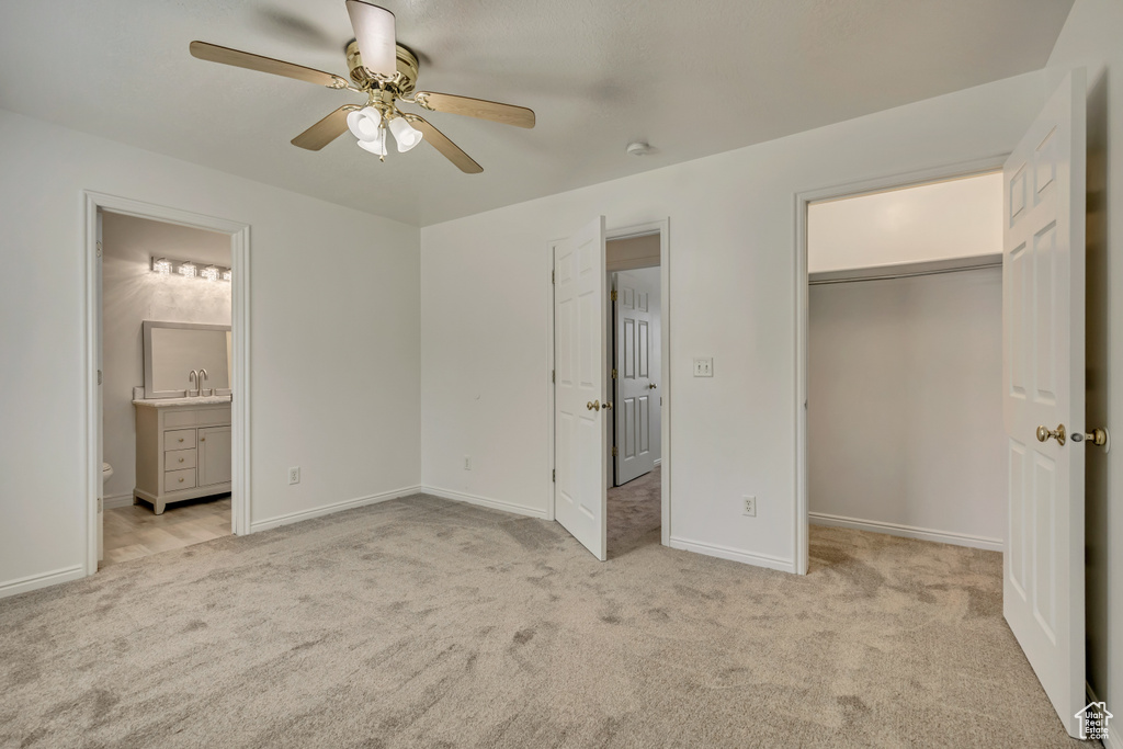 Unfurnished bedroom with a sink, light colored carpet, connected bathroom, and a walk in closet