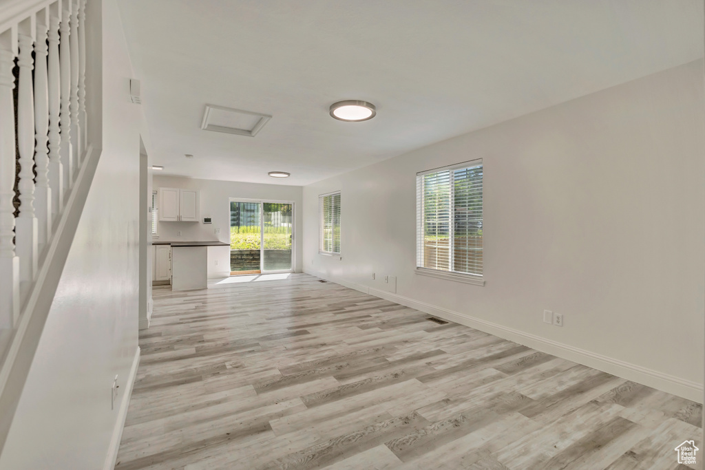Unfurnished living room with light wood-style floors, baseboards, and attic access