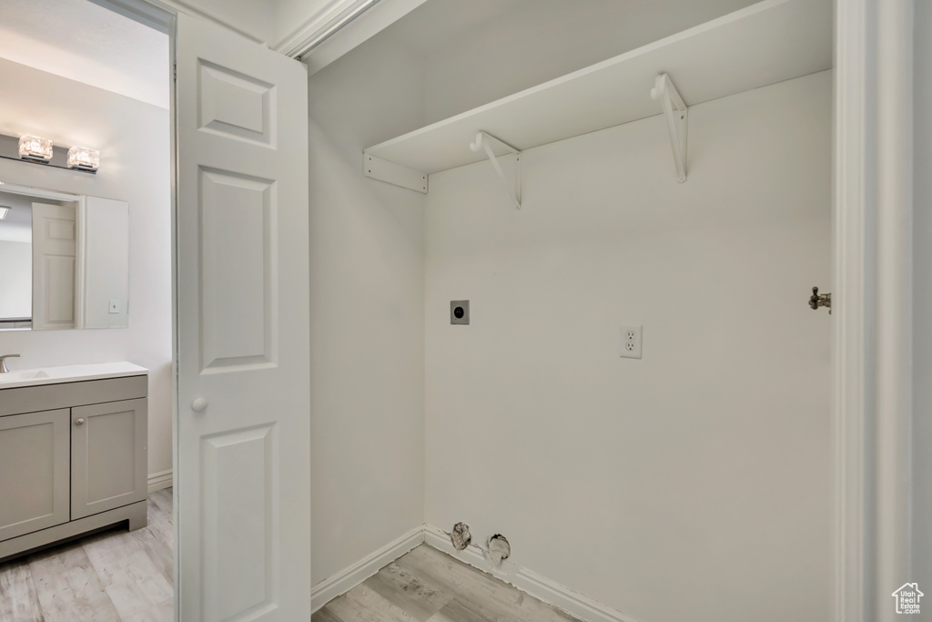 Laundry area featuring electric dryer hookup, light wood-type flooring, and baseboards