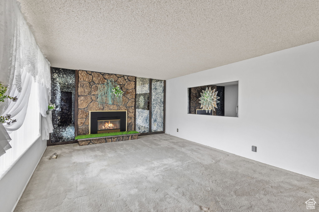 Unfurnished living room featuring carpet floors, a fireplace, and a textured ceiling