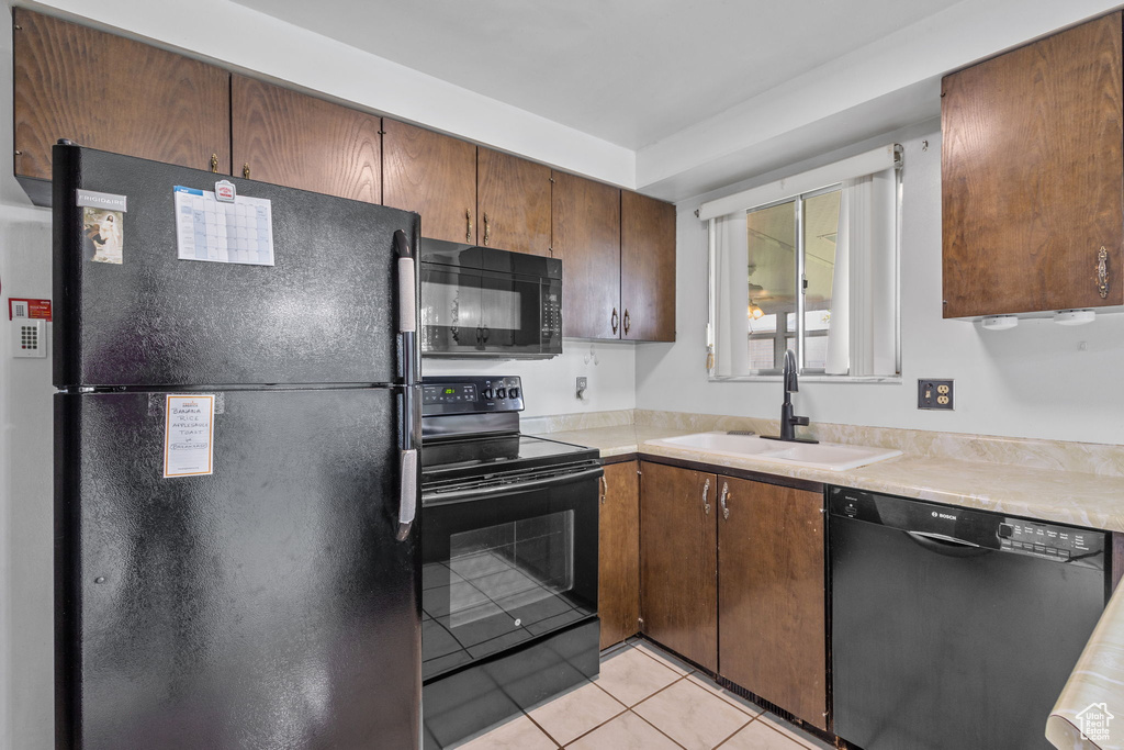 Kitchen with black appliances, a sink, light tile patterned flooring, and light countertops