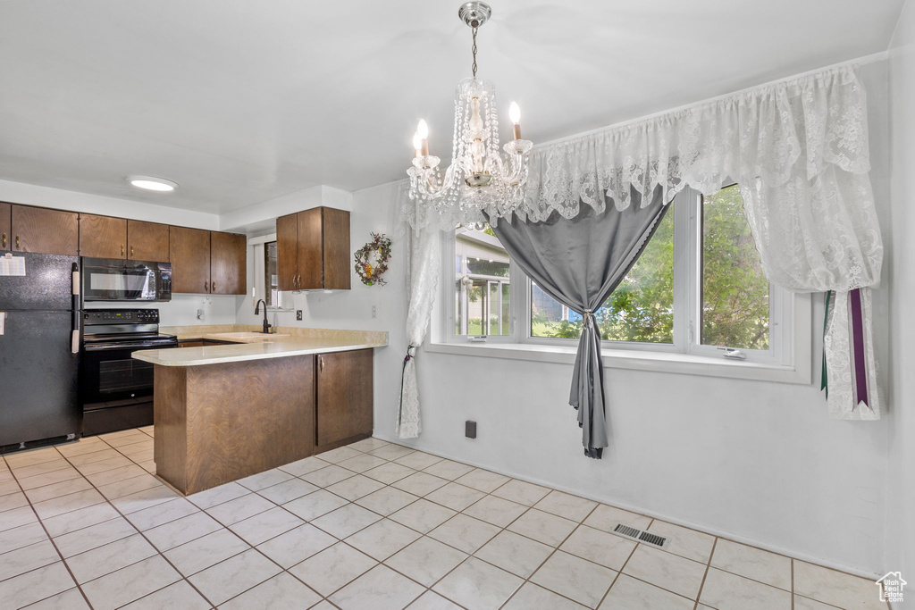 Kitchen with black appliances, a sink, light countertops, a peninsula, and a chandelier
