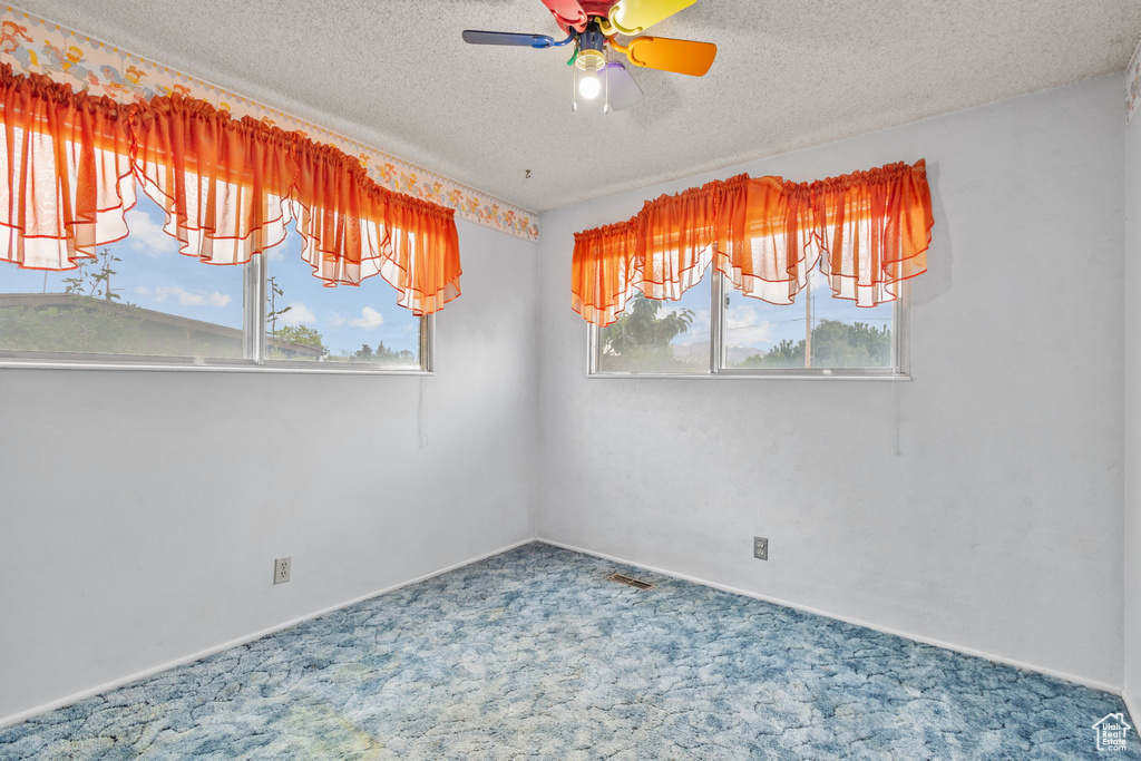 Carpeted empty room featuring ceiling fan, a textured ceiling, and baseboards