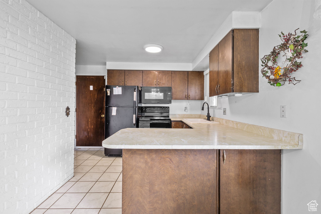 Kitchen with black appliances, a sink, light countertops, a peninsula, and light tile patterned floors