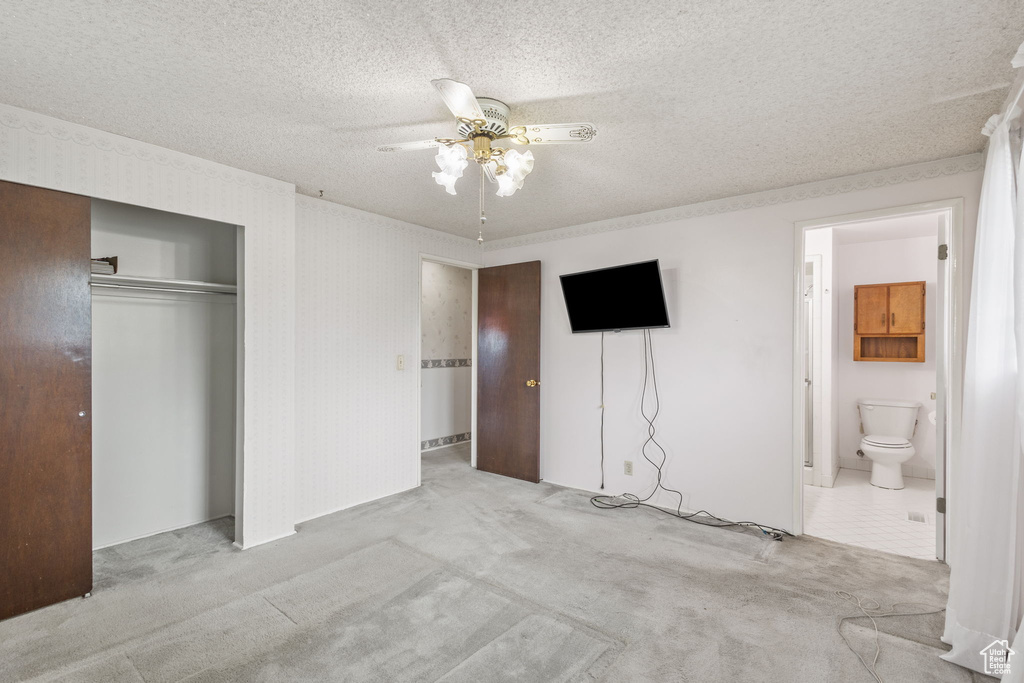 Unfurnished bedroom with carpet flooring, a textured ceiling, a closet, connected bathroom, and ceiling fan