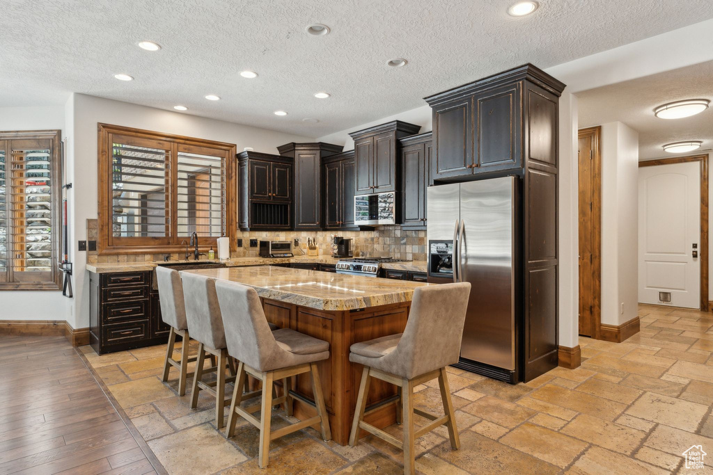 Kitchen featuring appliances with stainless steel finishes, baseboards, a kitchen breakfast bar, tasteful backsplash, and a kitchen island