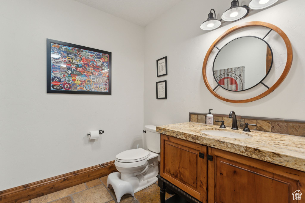 Bathroom featuring vanity, stone tile flooring, baseboards, and toilet