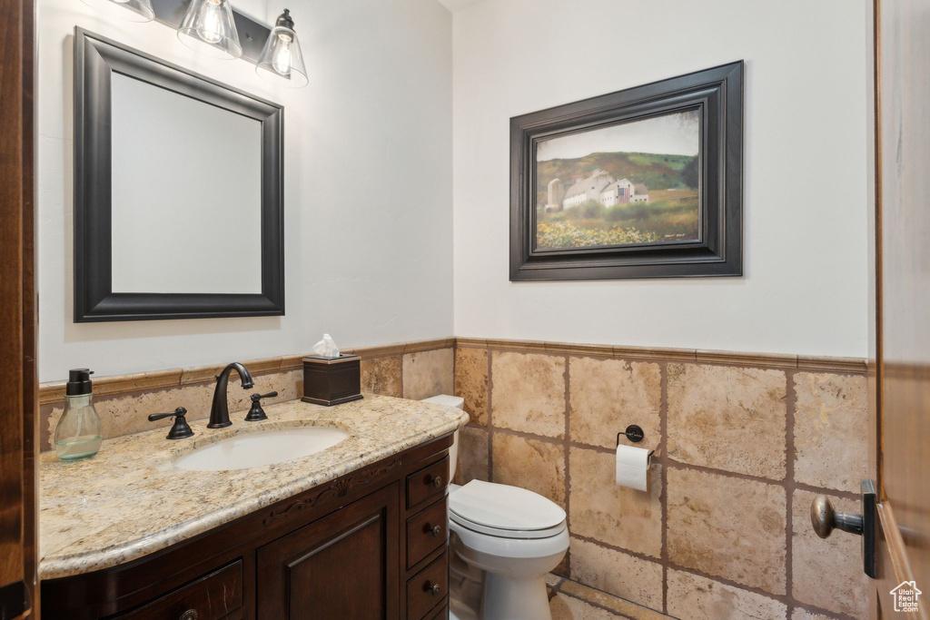 Half bath featuring vanity, toilet, wainscoting, and tile walls