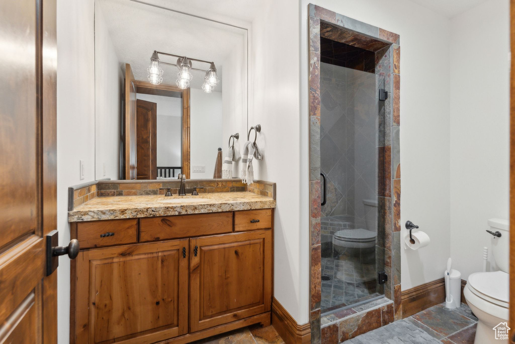 Bathroom featuring toilet, vanity, a shower stall, baseboards, and stone finish floors