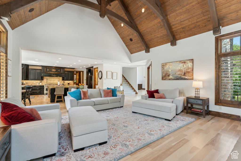 Living room with light wood finished floors, stairway, high vaulted ceiling, wood ceiling with exposed beams, and baseboards