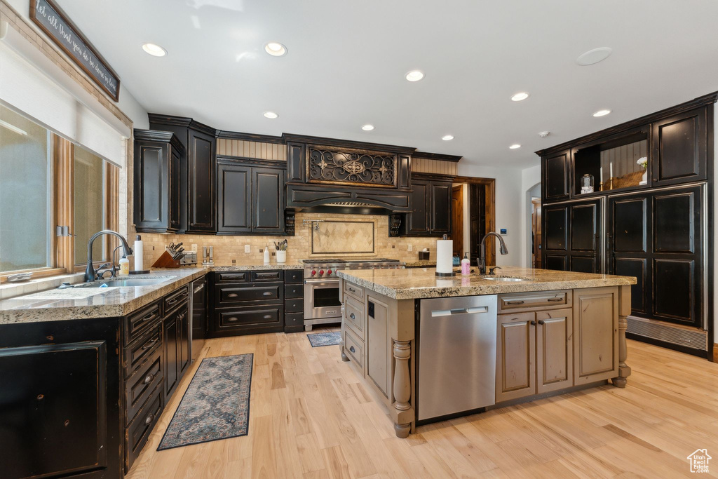 Kitchen featuring appliances with stainless steel finishes, light wood-style floors, a sink, tasteful backsplash, and light stone countertops