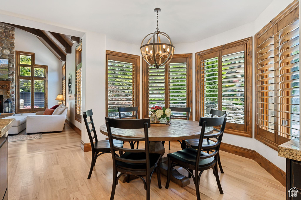 Dining space with a chandelier, light wood-style floors, baseboards, plenty of natural light, and vaulted ceiling