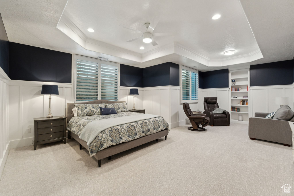 Bedroom with a raised ceiling, a decorative wall, crown molding, a wainscoted wall, and carpet flooring