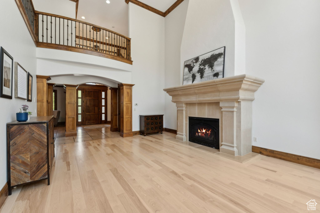 Unfurnished living room with ornate columns, arched walkways, wood finished floors, baseboards, and a warm lit fireplace