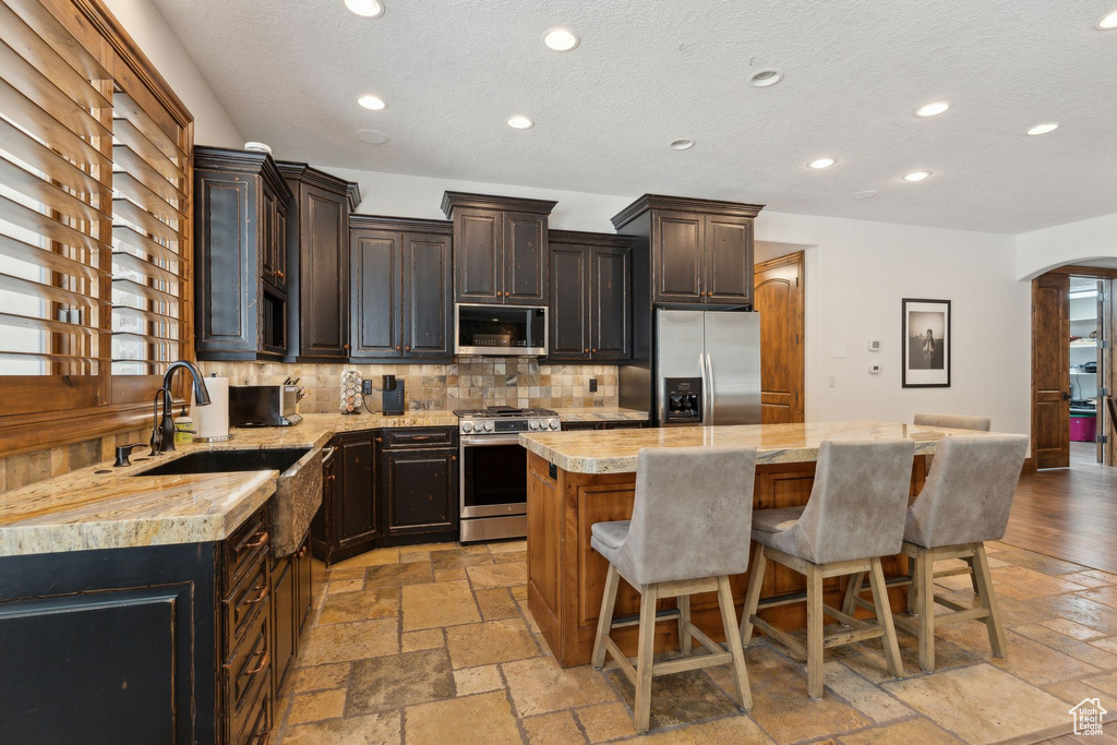 Kitchen with stainless steel appliances, a sink, a kitchen island, decorative backsplash, and a breakfast bar