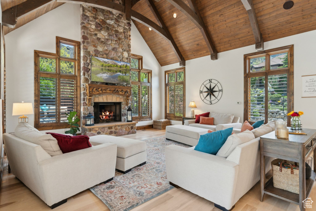 Living area with wooden ceiling with exposed beams, light wood-style flooring, healthy amount of natural light, high vaulted ceiling, and a fireplace