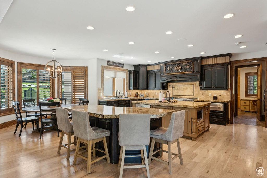 Kitchen with a center island with sink, a chandelier, a sink, stainless steel microwave, and tasteful backsplash