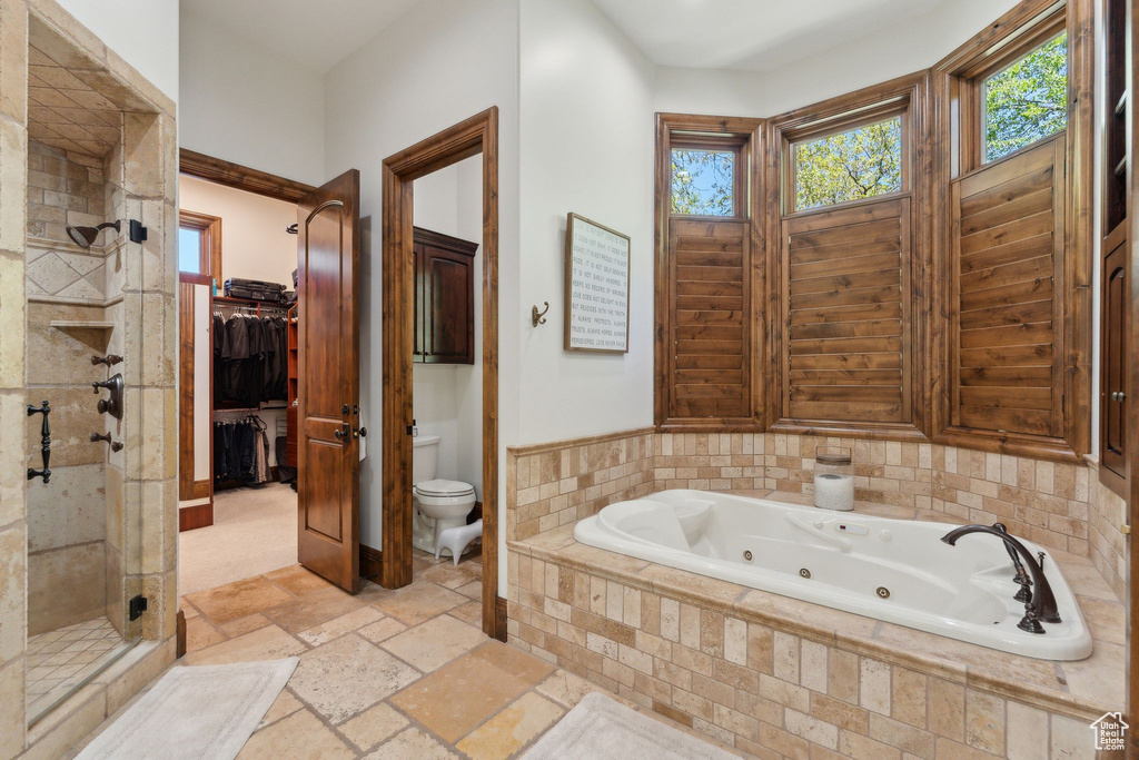 Full bathroom with a stall shower, a whirlpool tub, toilet, and stone tile floors