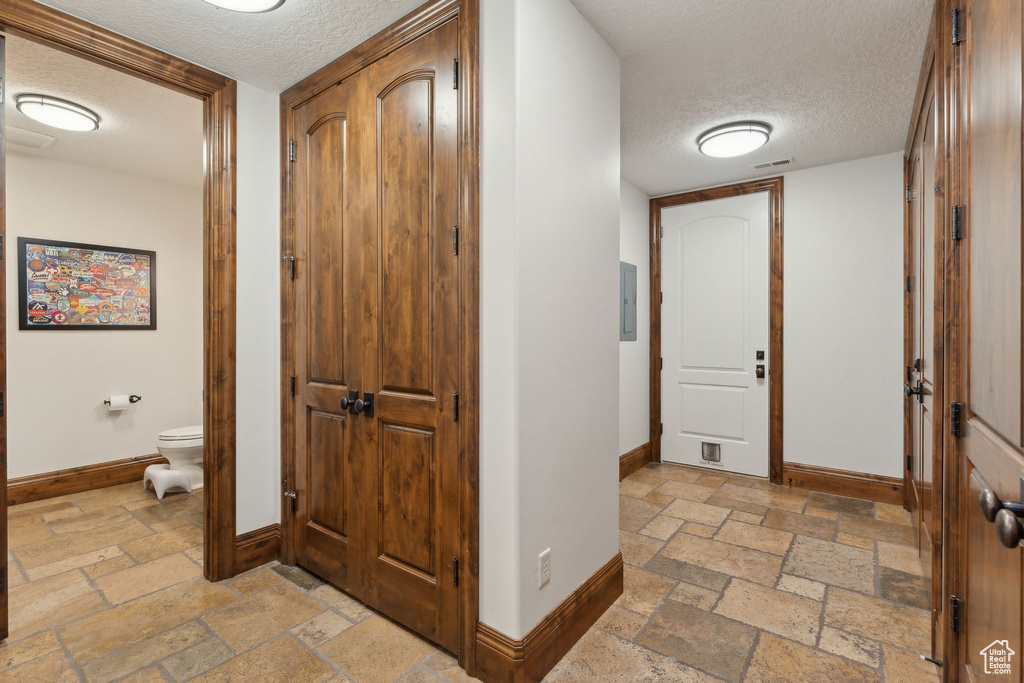 Hall with baseboards, a textured ceiling, stone tile floors, and electric panel