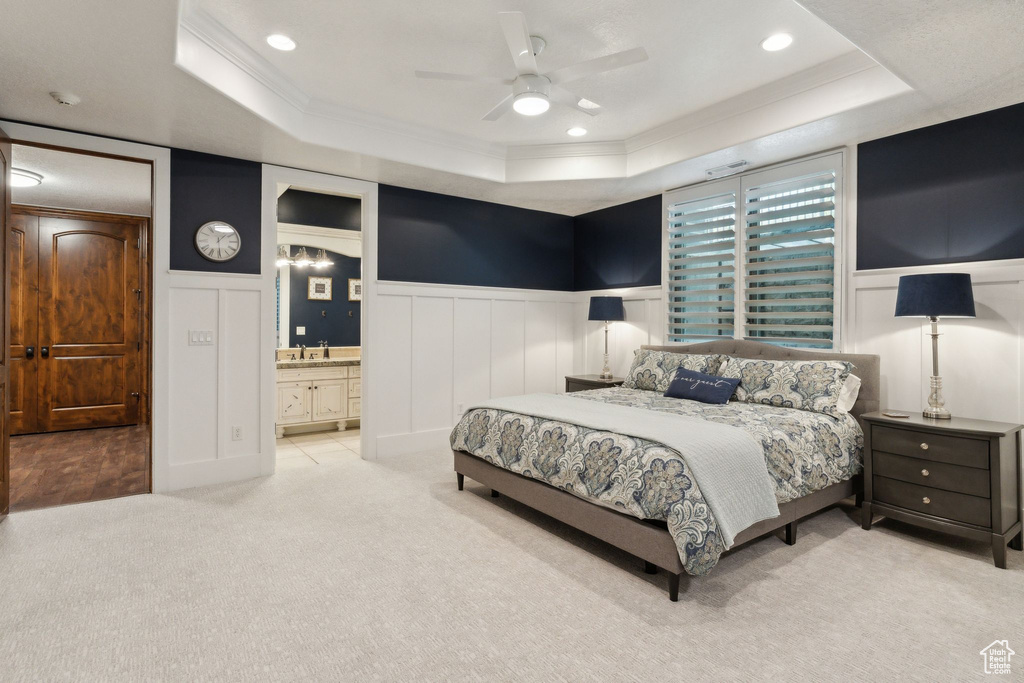 Bedroom featuring a tray ceiling, a decorative wall, ornamental molding, wainscoting, and carpet floors