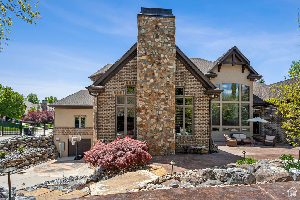 Back of property featuring a patio area, a chimney, brick siding, roof with shingles, and stucco siding
