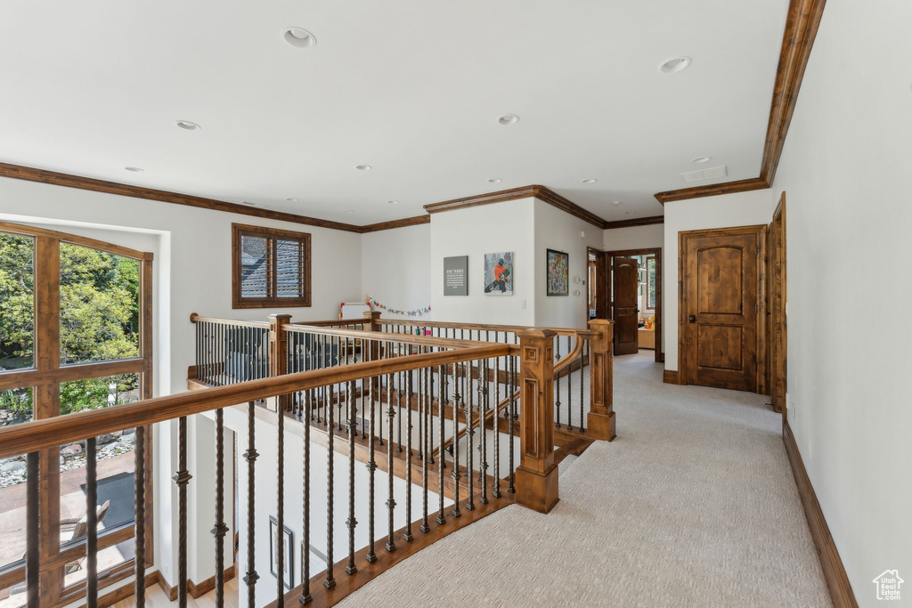 Hallway with an upstairs landing, light colored carpet, baseboards, recessed lighting, and crown molding