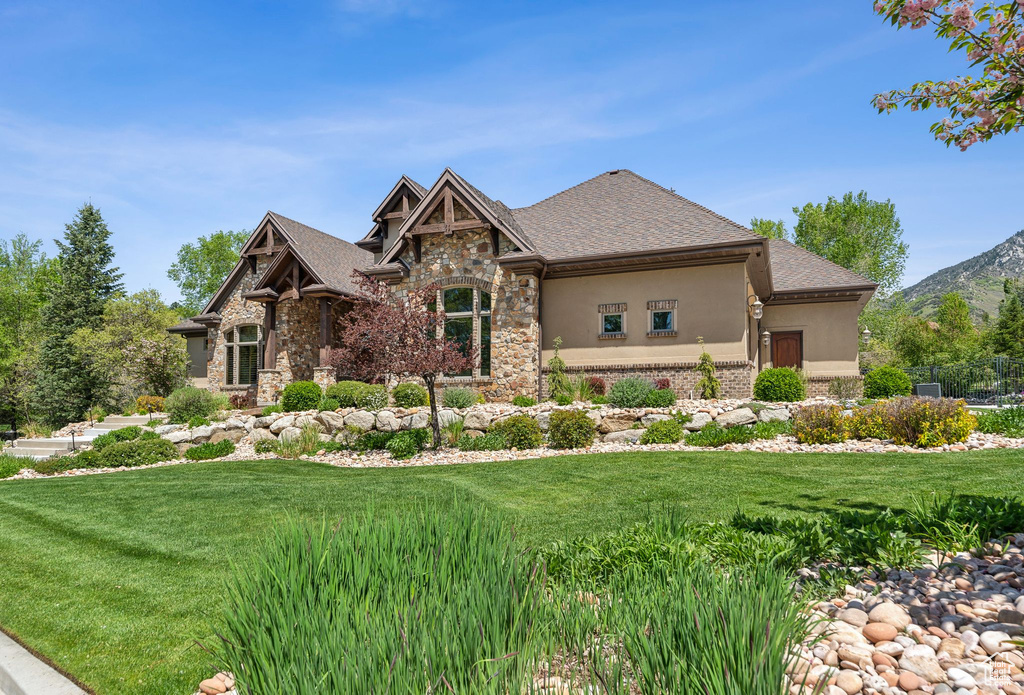 View of front of house with stone siding, stucco siding, a front lawn, and a mountain view