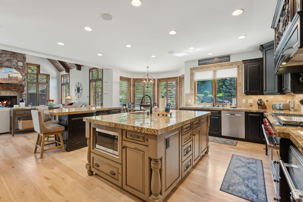 Kitchen featuring appliances with stainless steel finishes, an island with sink, recessed lighting, decorative backsplash, and light wood finished floors