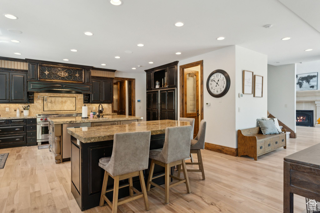 Kitchen with a kitchen island with sink, stainless steel range, a breakfast bar, decorative backsplash, and custom range hood