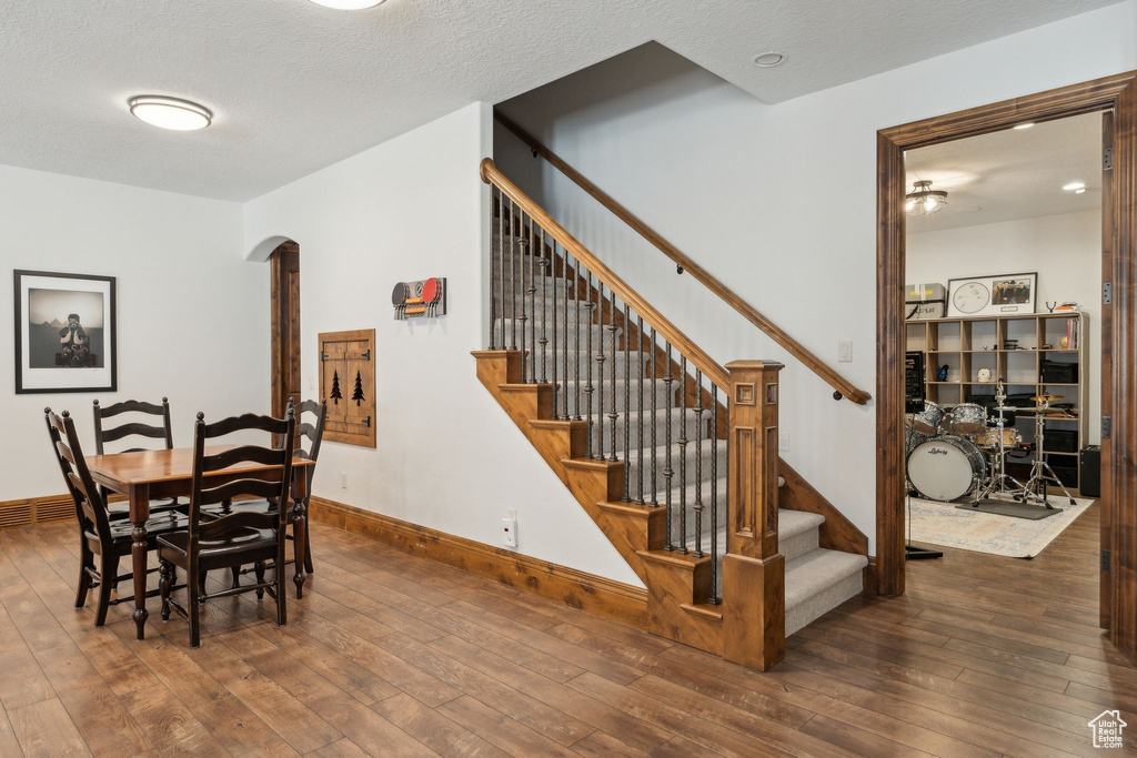 Dining space featuring arched walkways, hardwood / wood-style flooring, stairs, and a textured ceiling