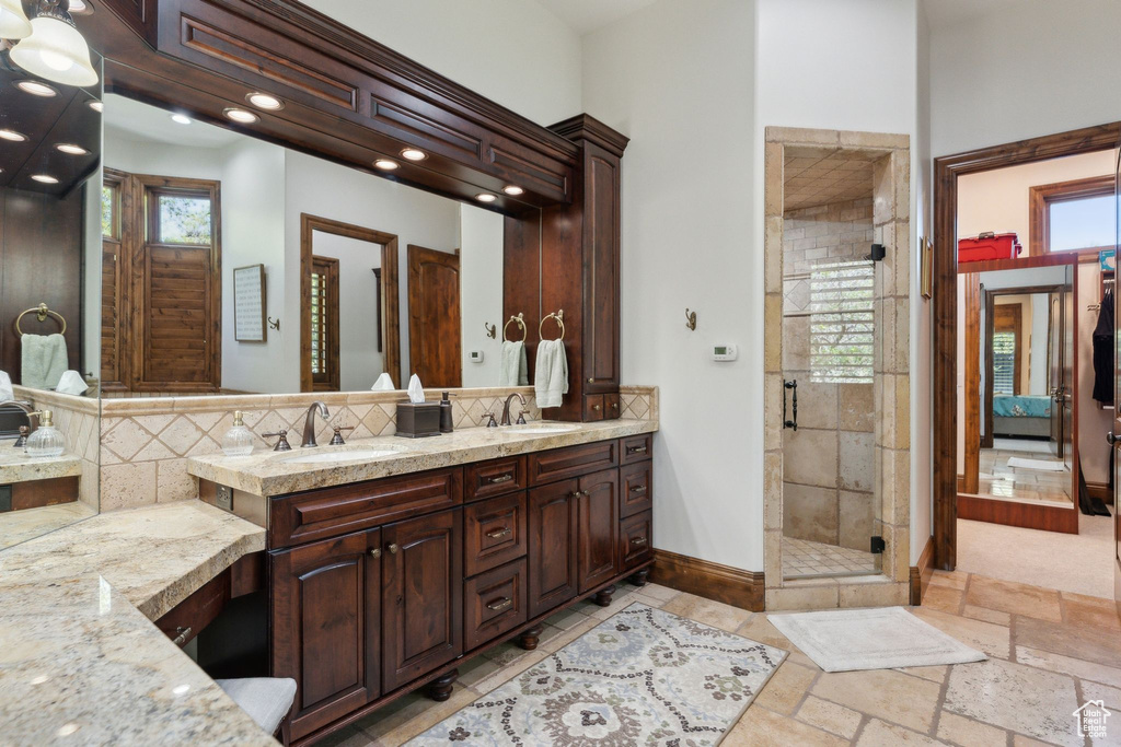 Bathroom featuring double vanity, a shower stall, backsplash, baseboards, and recessed lighting
