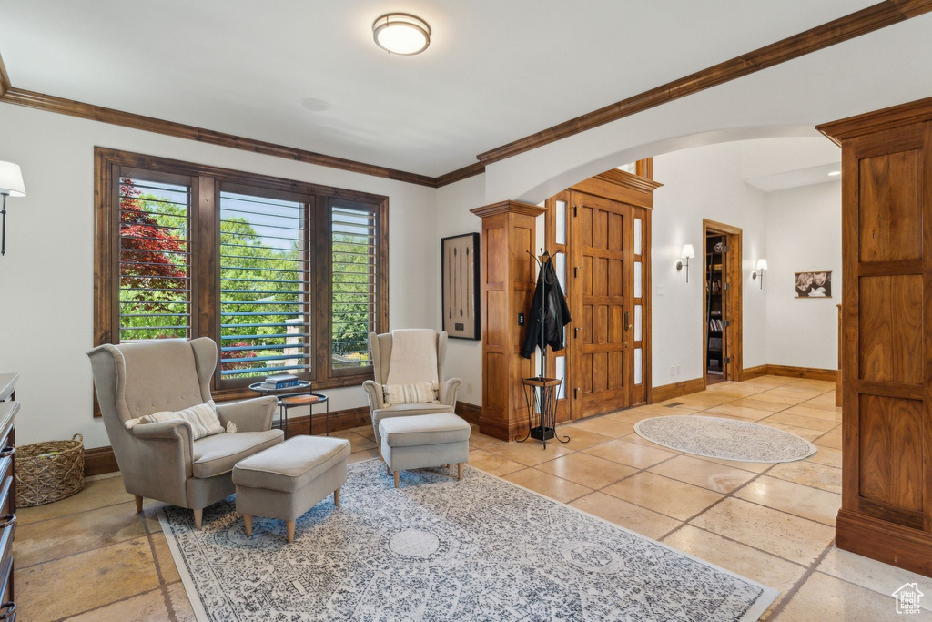 Living area with arched walkways, ornate columns, ornamental molding, baseboards, and light tile patterned floors