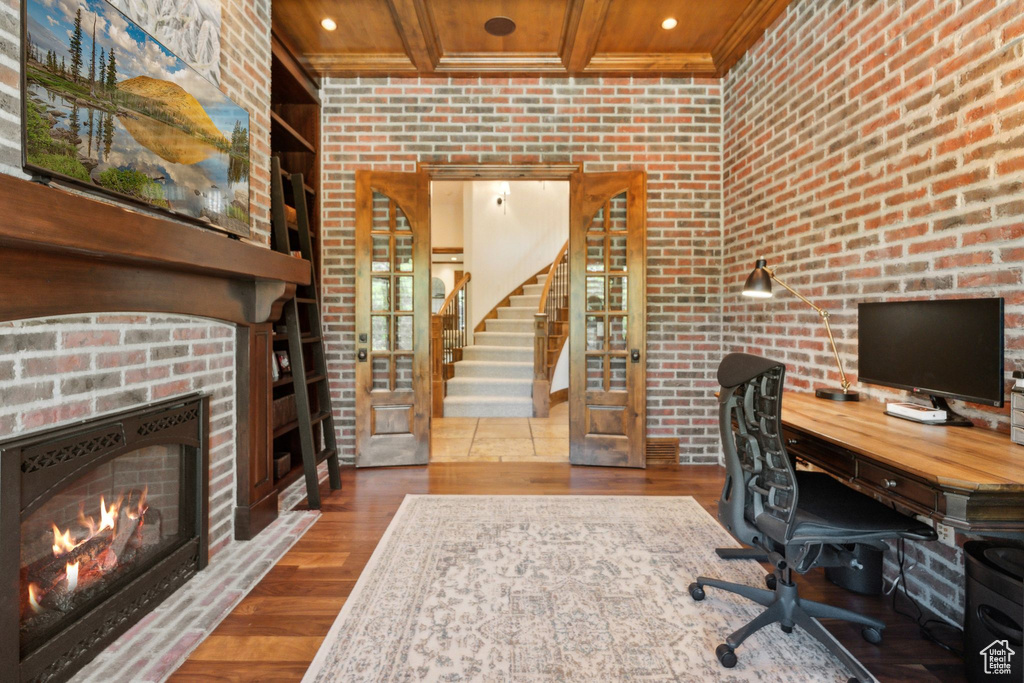Office space with a lit fireplace, wood finished floors, brick wall, wooden ceiling with exposed beams, and recessed lighting