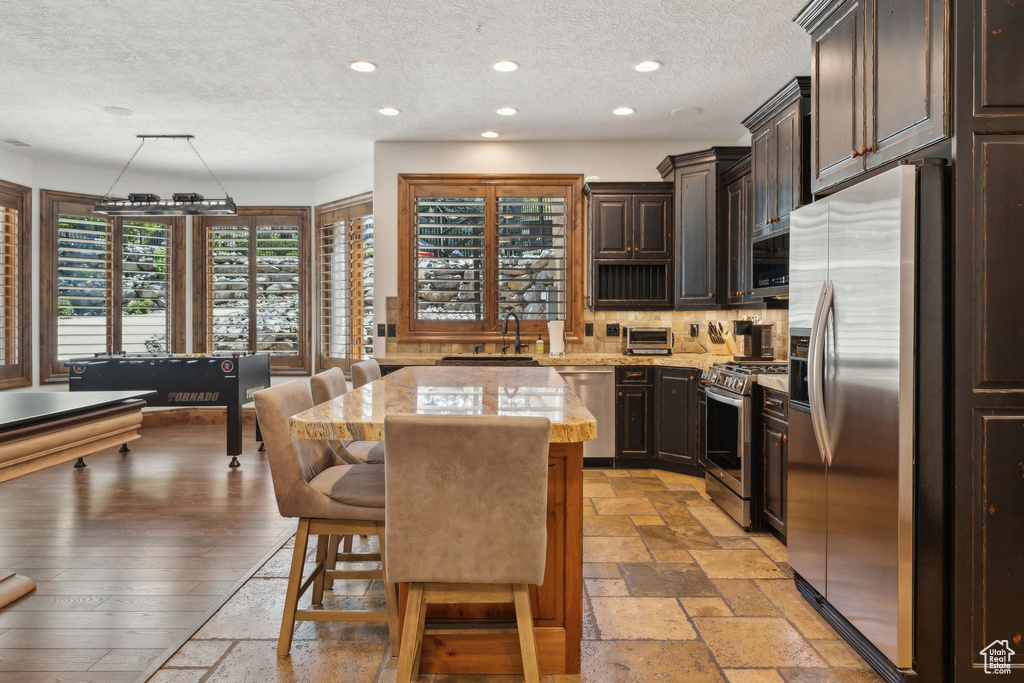 Kitchen with stainless steel appliances, a sink, a textured ceiling, a center island, and light stone countertops