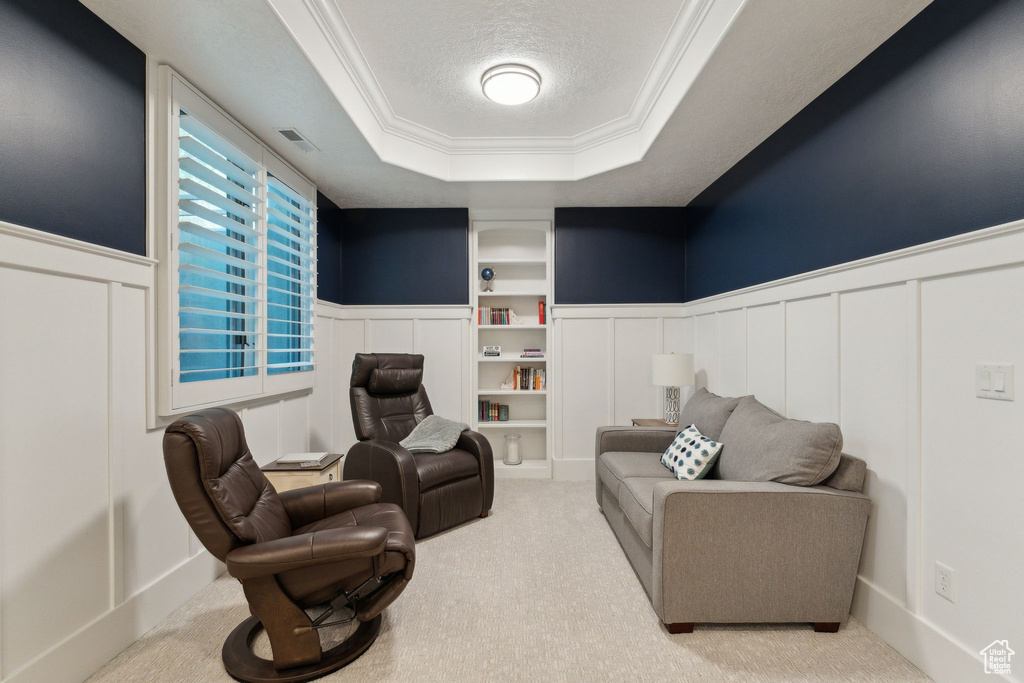 Living area with a decorative wall, a raised ceiling, ornamental molding, a wainscoted wall, and carpet flooring