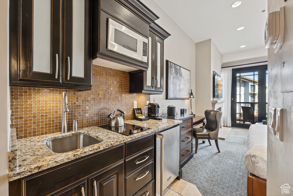 Kitchen featuring a sink, dark brown cabinets, stainless steel microwave, decorative backsplash, and black electric stovetop