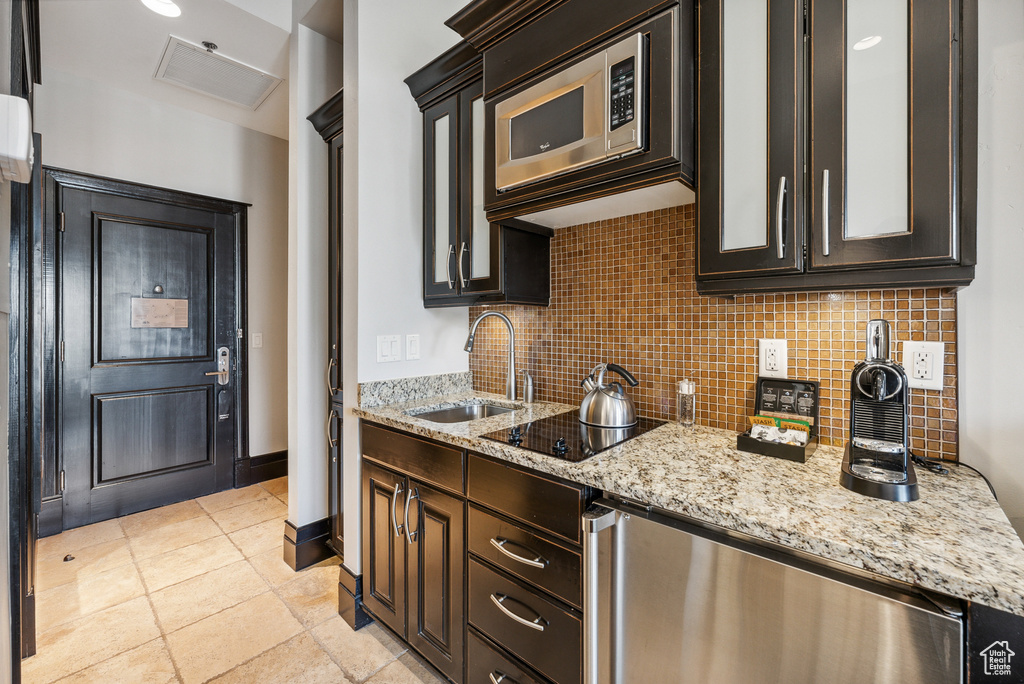 Kitchen with a sink, stainless steel microwave, tasteful backsplash, and black electric stovetop