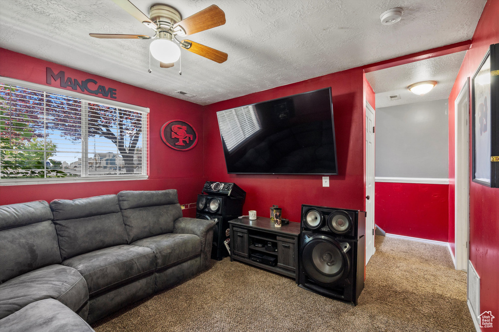 Carpeted living area featuring ceiling fan and a textured ceiling
