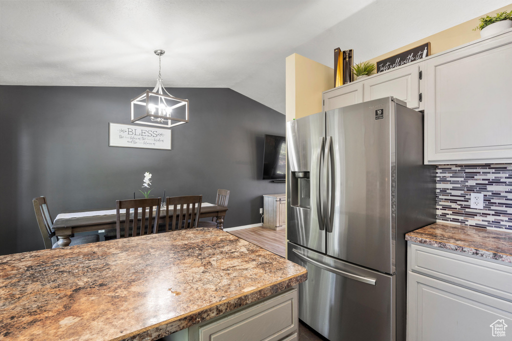 Kitchen with stainless steel fridge with ice dispenser, decorative backsplash, a chandelier, vaulted ceiling, and white cabinetry