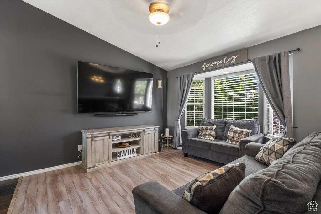 Living room featuring lofted ceiling, light wood-style flooring, a ceiling fan, and baseboards