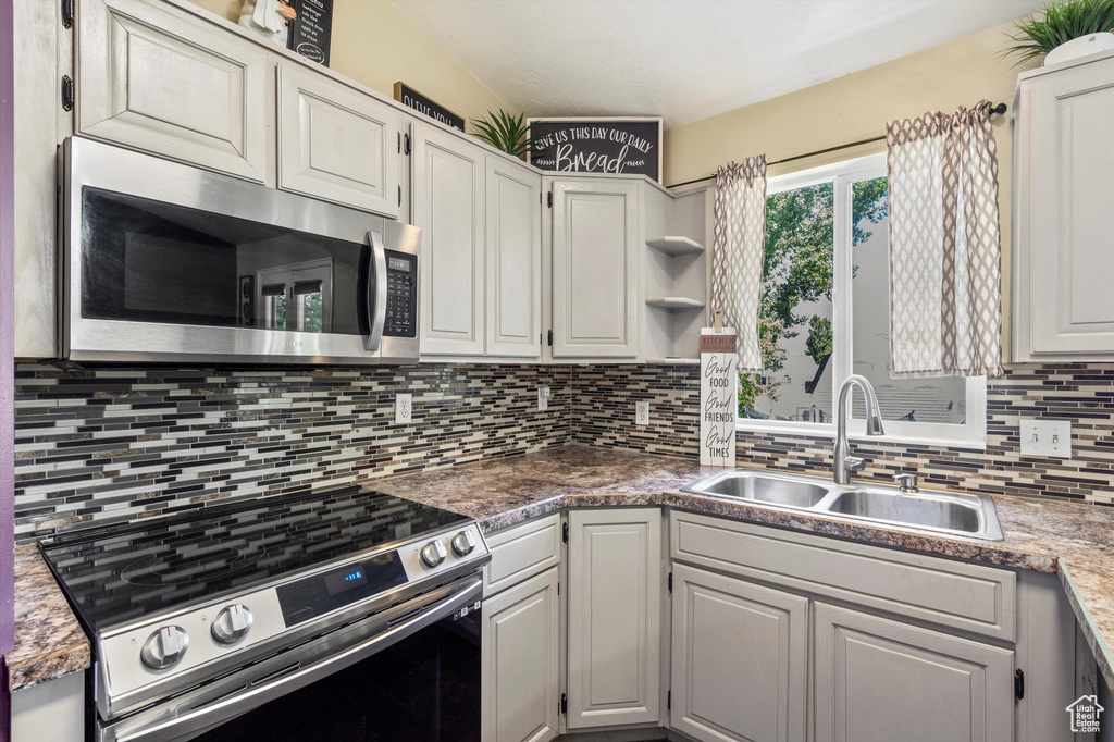 Kitchen featuring stainless steel appliances, a sink, tasteful backsplash, open shelves, and white cabinetry