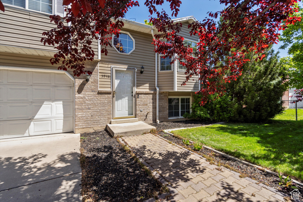 View of front of house with a front yard, stone siding, a garage, and concrete driveway