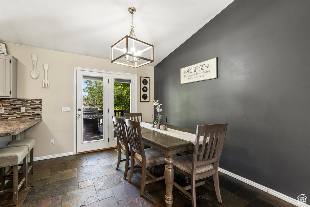 Dining space with a chandelier, lofted ceiling, baseboards, and stone tile flooring