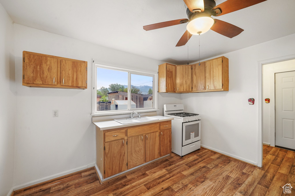 Kitchen featuring white range with gas cooktop, a sink, light countertops, a ceiling fan, and wood finished floors