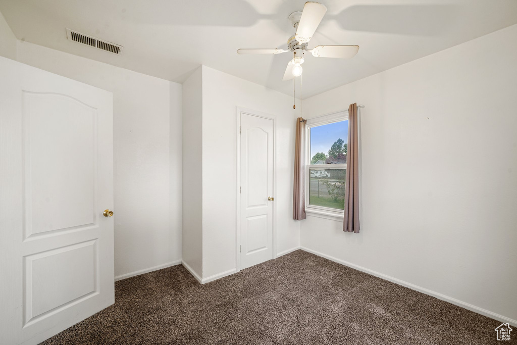 Spare room featuring dark colored carpet, baseboards, and ceiling fan