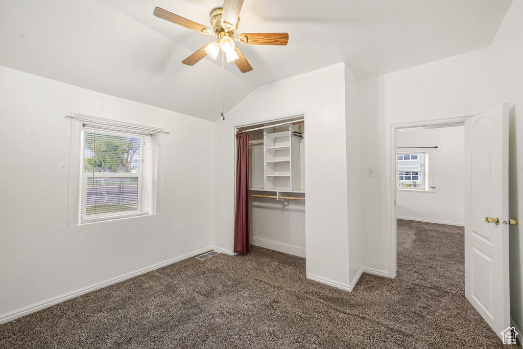 Unfurnished bedroom featuring dark colored carpet, multiple windows, lofted ceiling, baseboards, and a ceiling fan